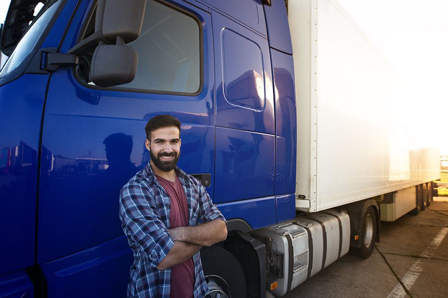 Specialized Business Insurance - Portrait of a Young Smiling Truck Driver Standing Next to His Blue Truck in a Parking Lot